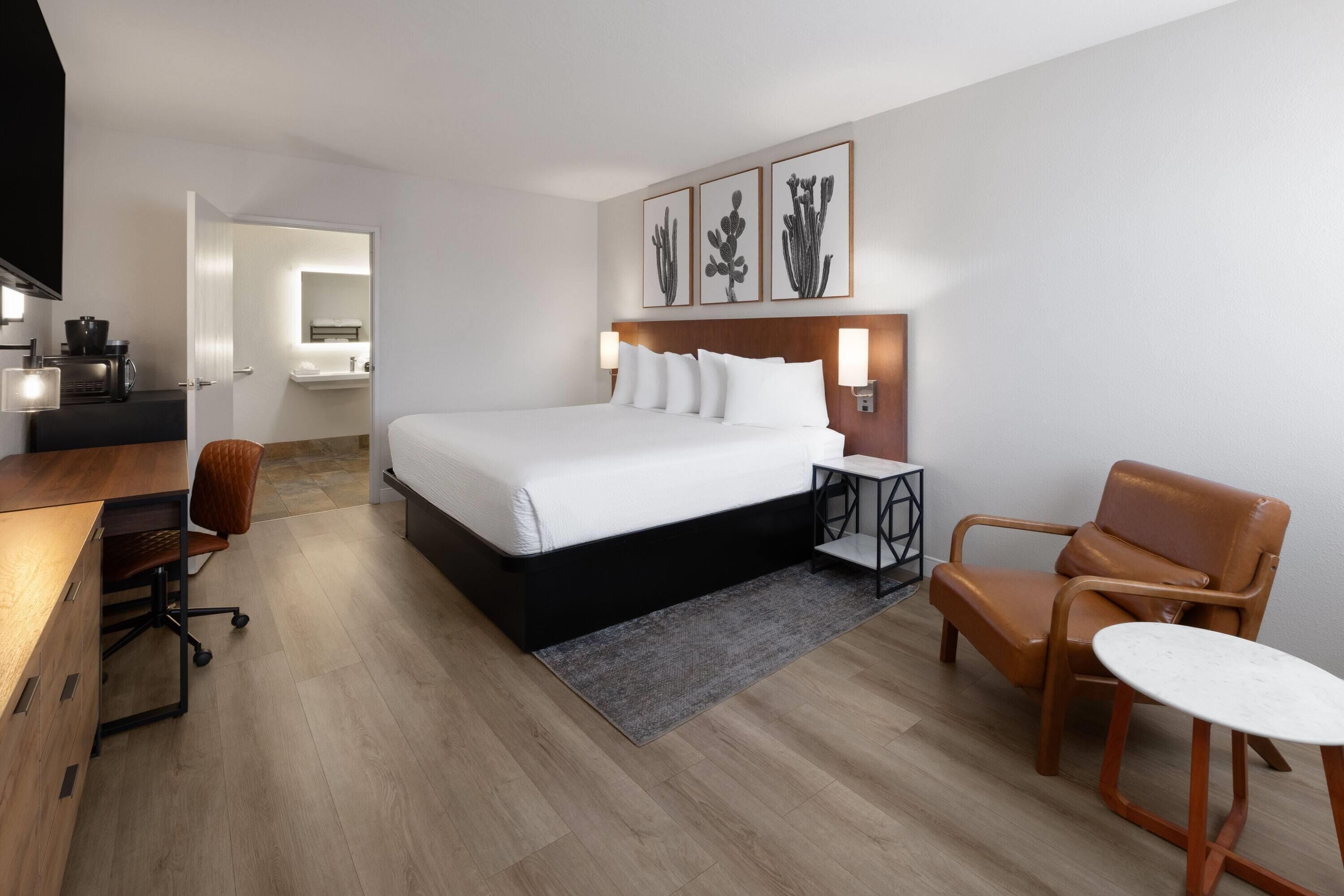 A modern hotel room with a large bed, a desk, a chair, and a small table.