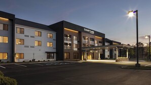 Un hotel Courtyard by Marriott con un diseño moderno, múltiples balcones y una entrada bien iluminada.