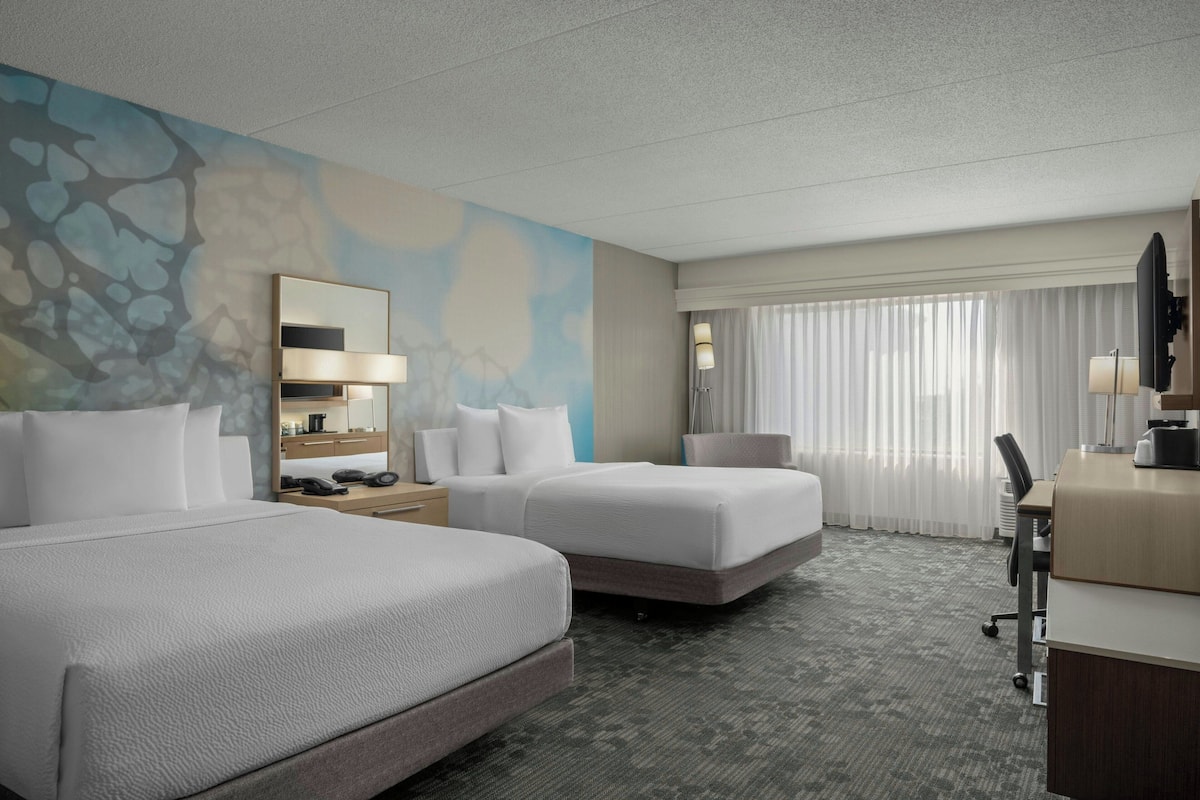 A hotel room with two beds, a desk, a chair, a TV, and a window with curtains.