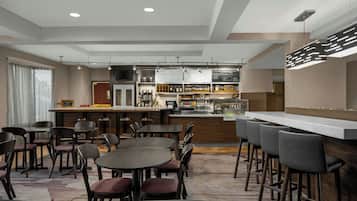 A modern hotel lobby with a bar area, seating arrangements, and a menu board.