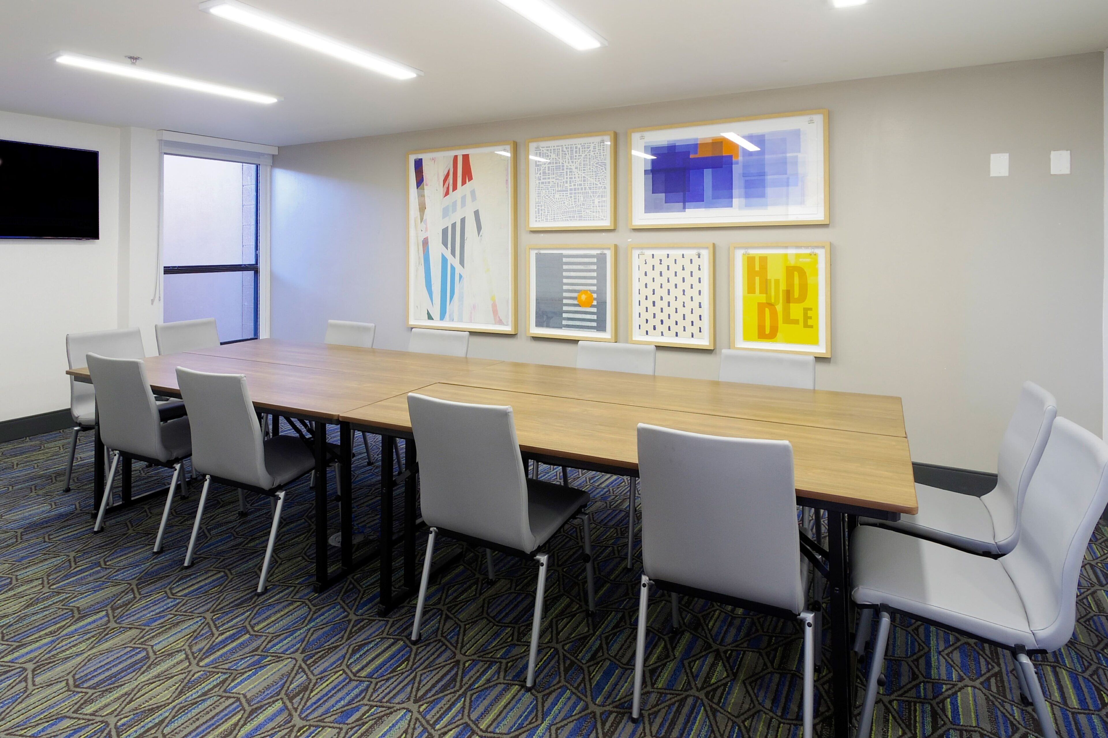 Uma sala de conferências com uma mesa comprida, seis cadeiras e seis obras de arte emolduradas na parede.
