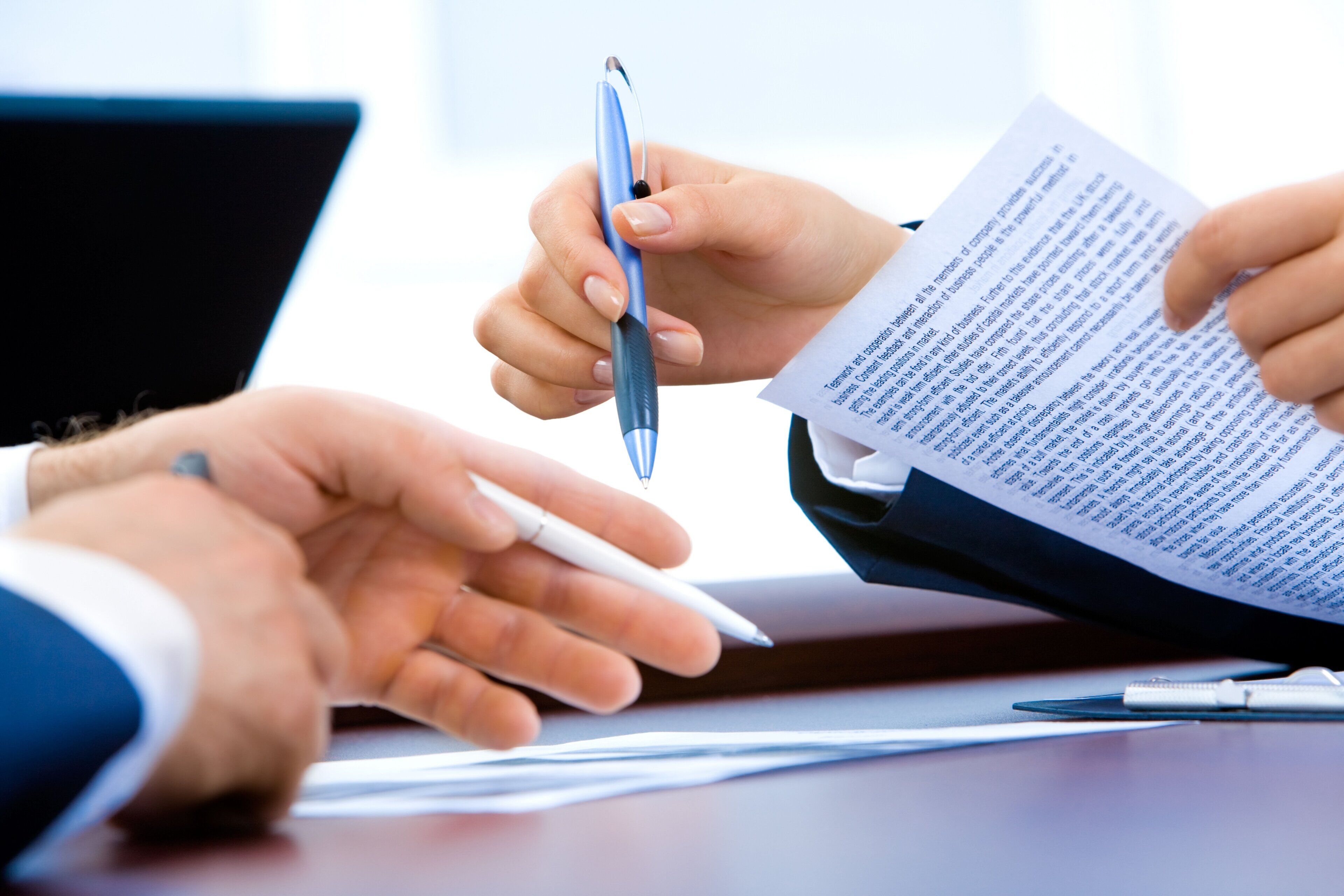 Una persona sosteniendo un bolígrafo y un documento, con la mano de otra persona a la vista.