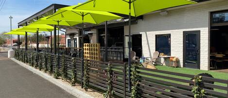A building with outdoor seating under bright yellow umbrellas, a white brick exterior, and a gravel pathway.
