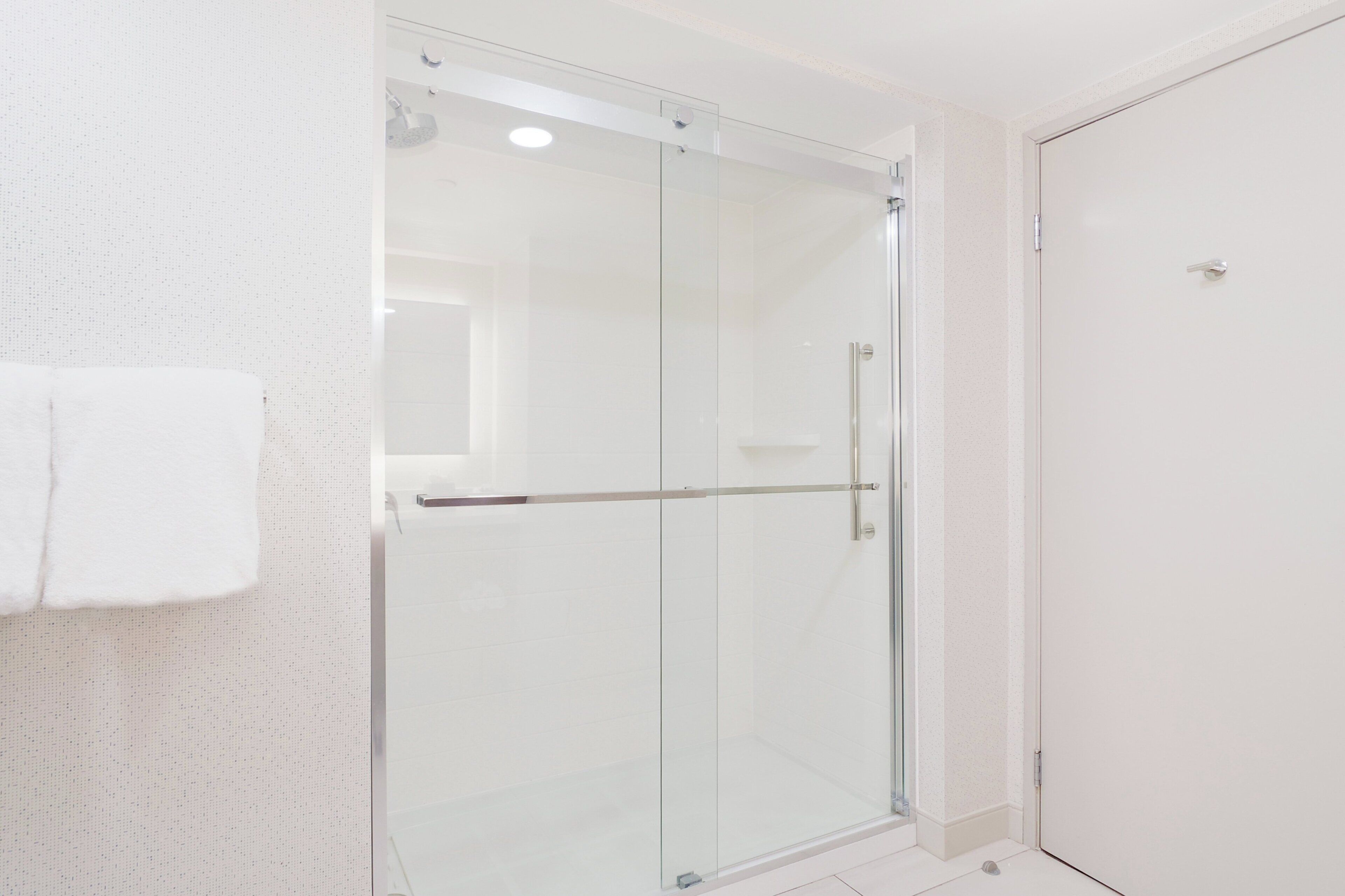 A modern bathroom with a glass shower enclosure, a white towel hanging on the wall, and a plain white door.
