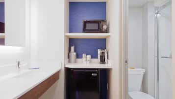 Un baño pequeño con un lavamanos blanco, un microondas en un estante, una cafetera y un inodoro con cabina de ducha.