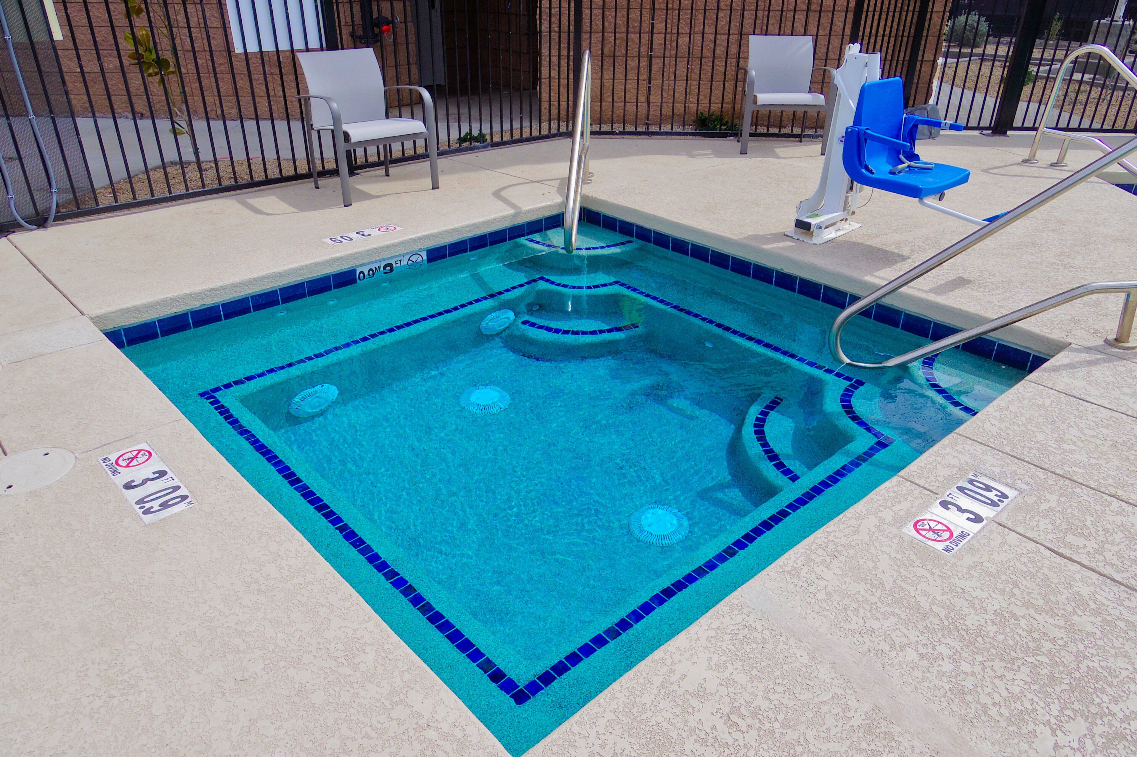 A swimming pool with a blue tiled border, a diving board, and two lounge chairs.