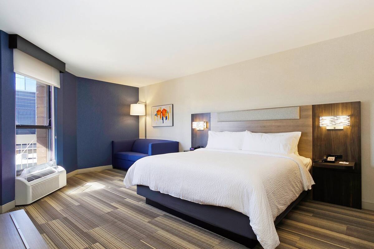 Une chambre d’hôtel moderne dotée d’un grand lit, d’un coin salon et d ’une fenêtre avec stores.