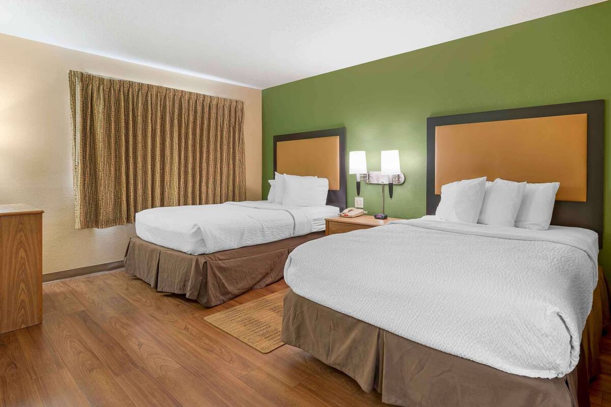Una camera d'albergo con due letti, una scrivania in legno e una parete decorata in verde.