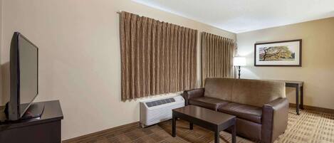 Habitación de hotel con sofá de cuero marrón, una mesita de centro, un televisor de pantalla plana sobre un soporte, aire acondicionado instalado en la pared y un cuadro enmarcado.