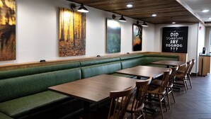 A restaurant with green cushioned booths, wooden tables, and artwork on the walls. - Fairfield Inn & Suites by Marriott Louisville Airport (Louisville)