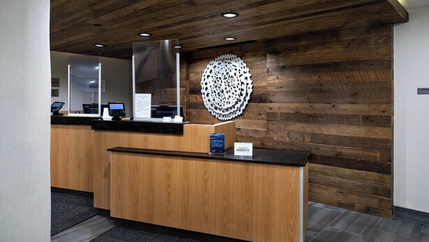 A reception desk with a wooden panel wall, a circular decorative piece, and a sign indicating 'Marriott Bonvoy'. - Fairfield Inn & Suites by Marriott Louisville Airport (Louisville)