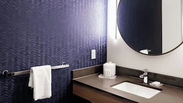 Un baño moderno con una pared de tono oscuro y estampado, un espejo redondo, un lavabo blanco y un perchero para toallas.