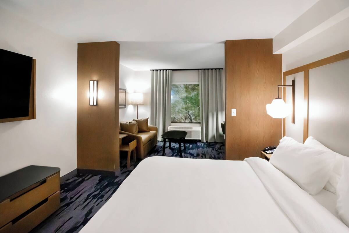 A hotel room with a large bed, a desk, a chair, and a window with curtains.