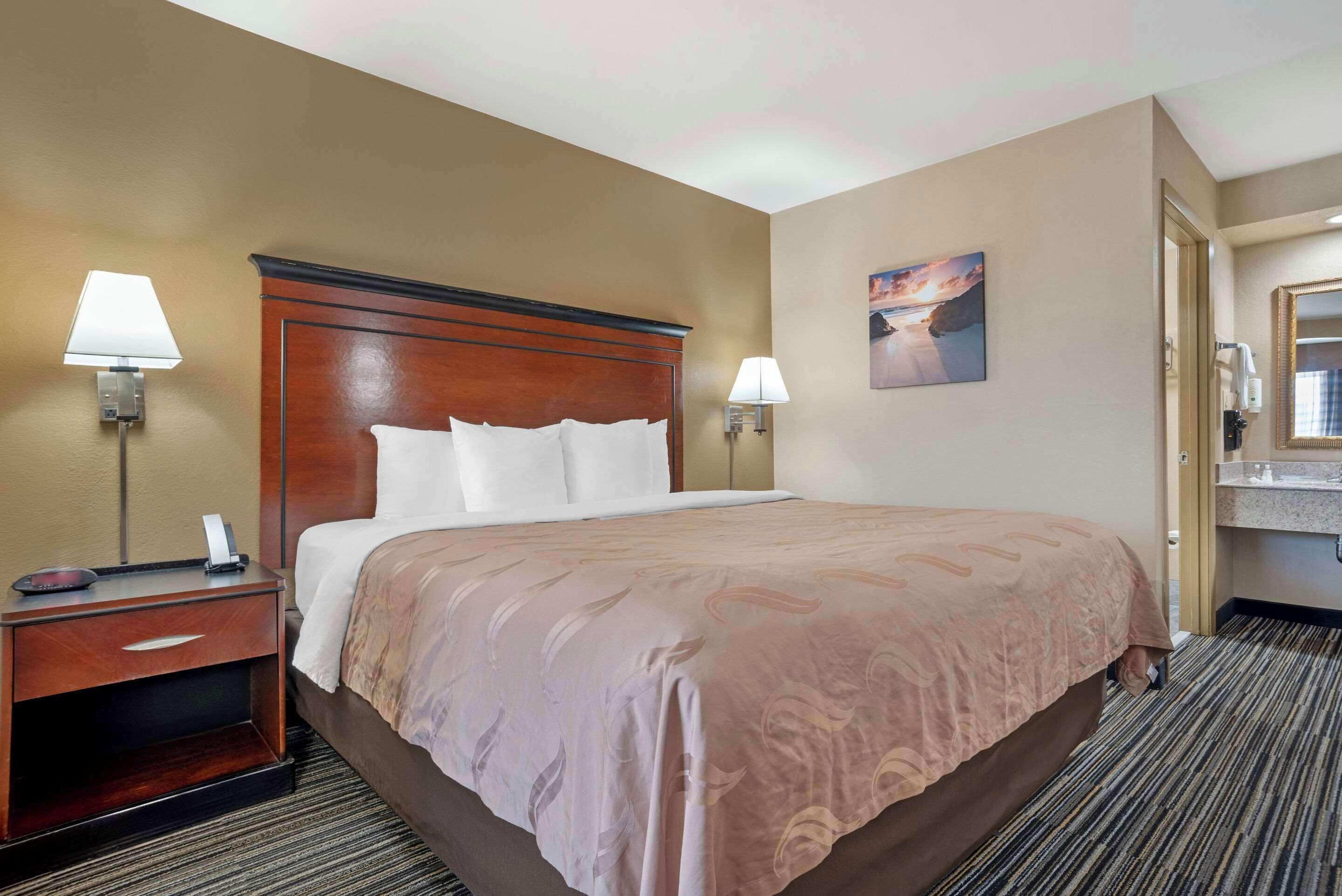 A hotel room with a large bed, two bedside lamps, a nightstand, and a painting on the wall.
