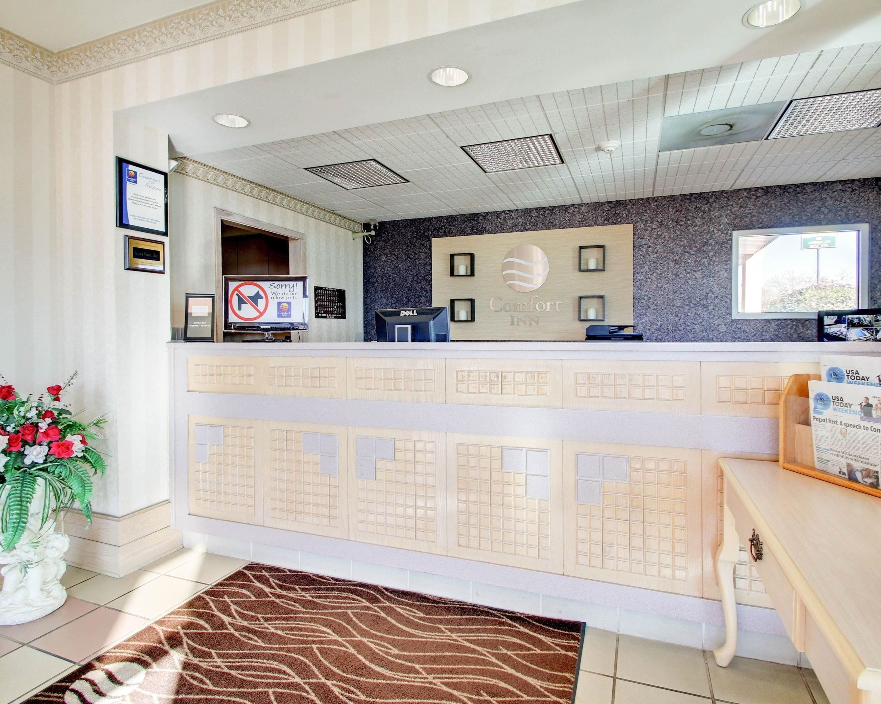 A hotel reception area with a desk, a computer, and a sign indicating no pets allowed.