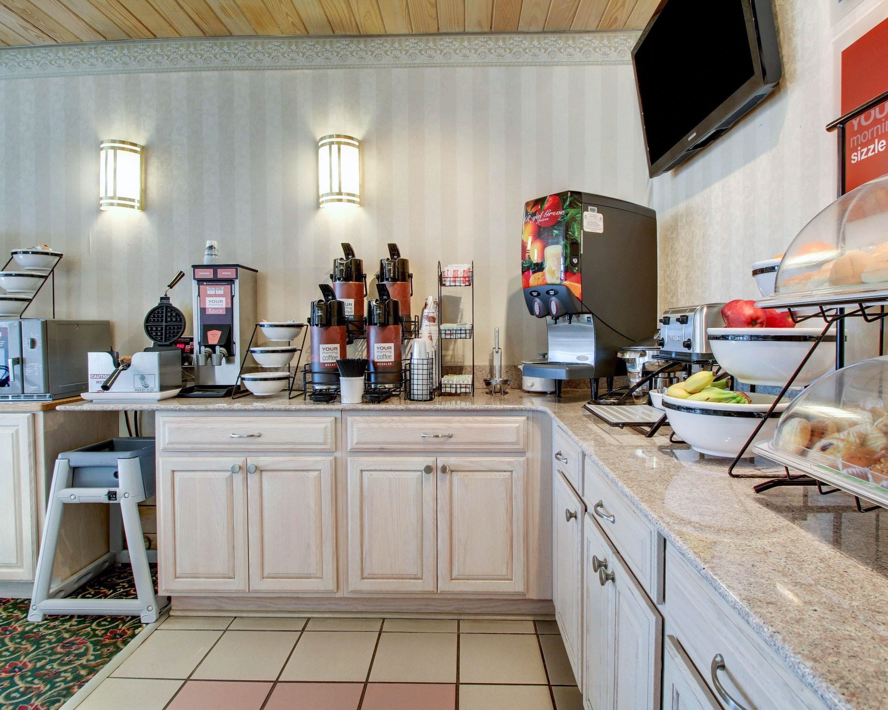 Ein Frühstücksbuffet mit Kaffeeautomaten, einem Waffeleisen und einer Obstauslage.