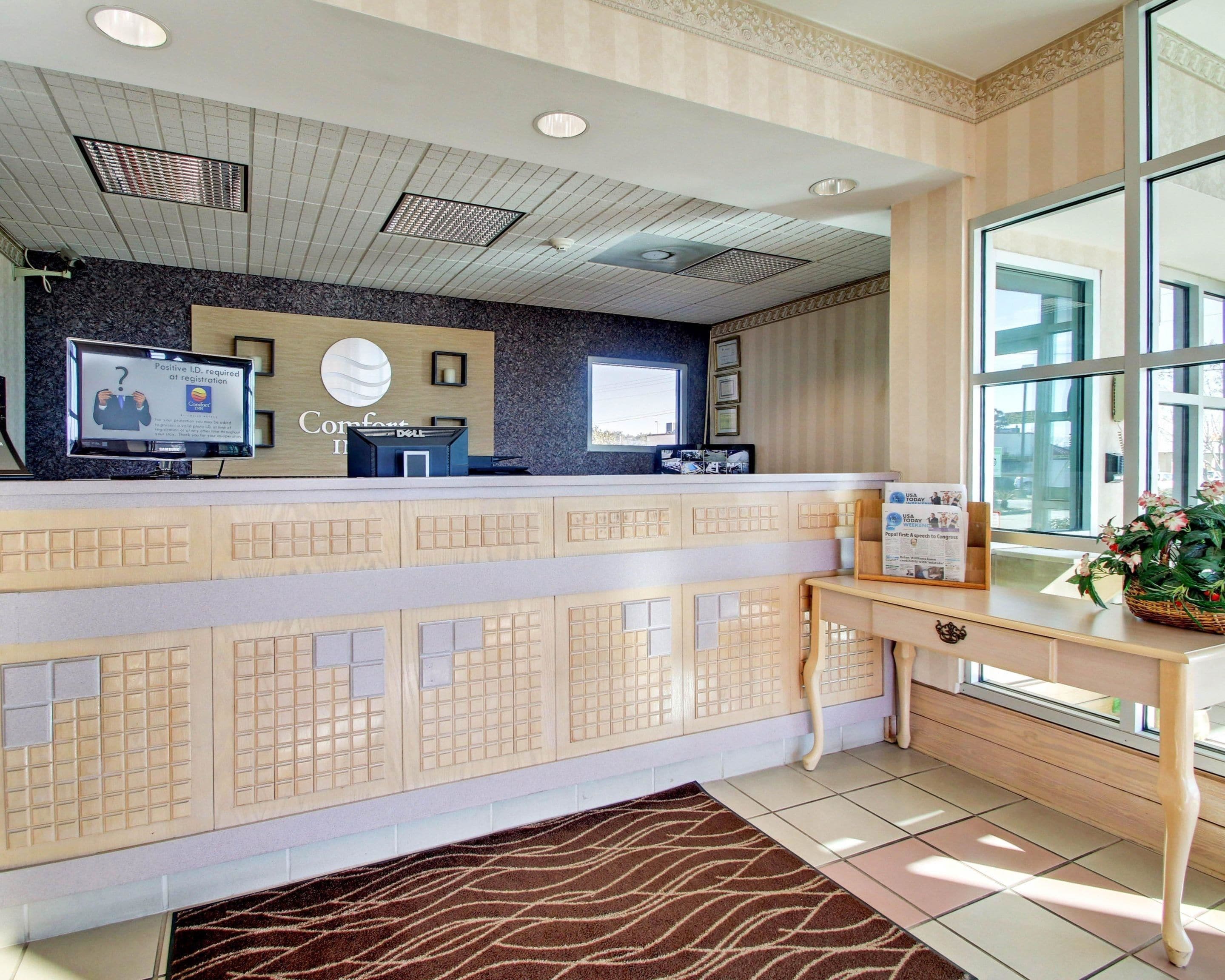 Ein Hotel-Empfangsbereich mit modernem Design, inklusive einer Rezeption, einem Flachbildfernseher, einer digitalen Anzeige und einem Fenster mit Blick.