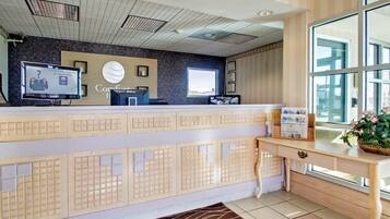 A hotel reception area with a modern design, featuring a reception desk, a flat-screen TV, a digital display, and a window with a view.