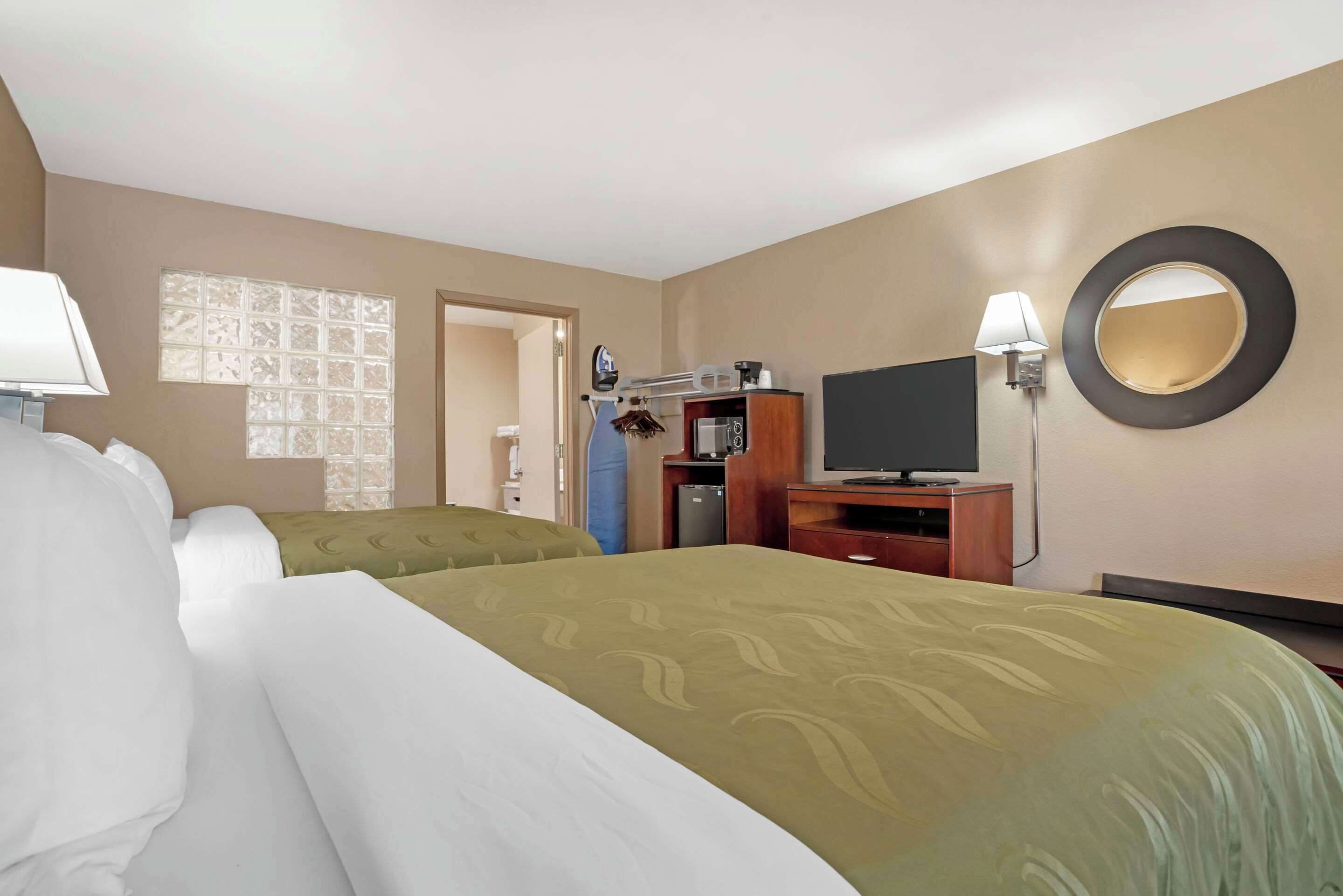 A hotel room with two beds, a television, a desk, and a mirror.