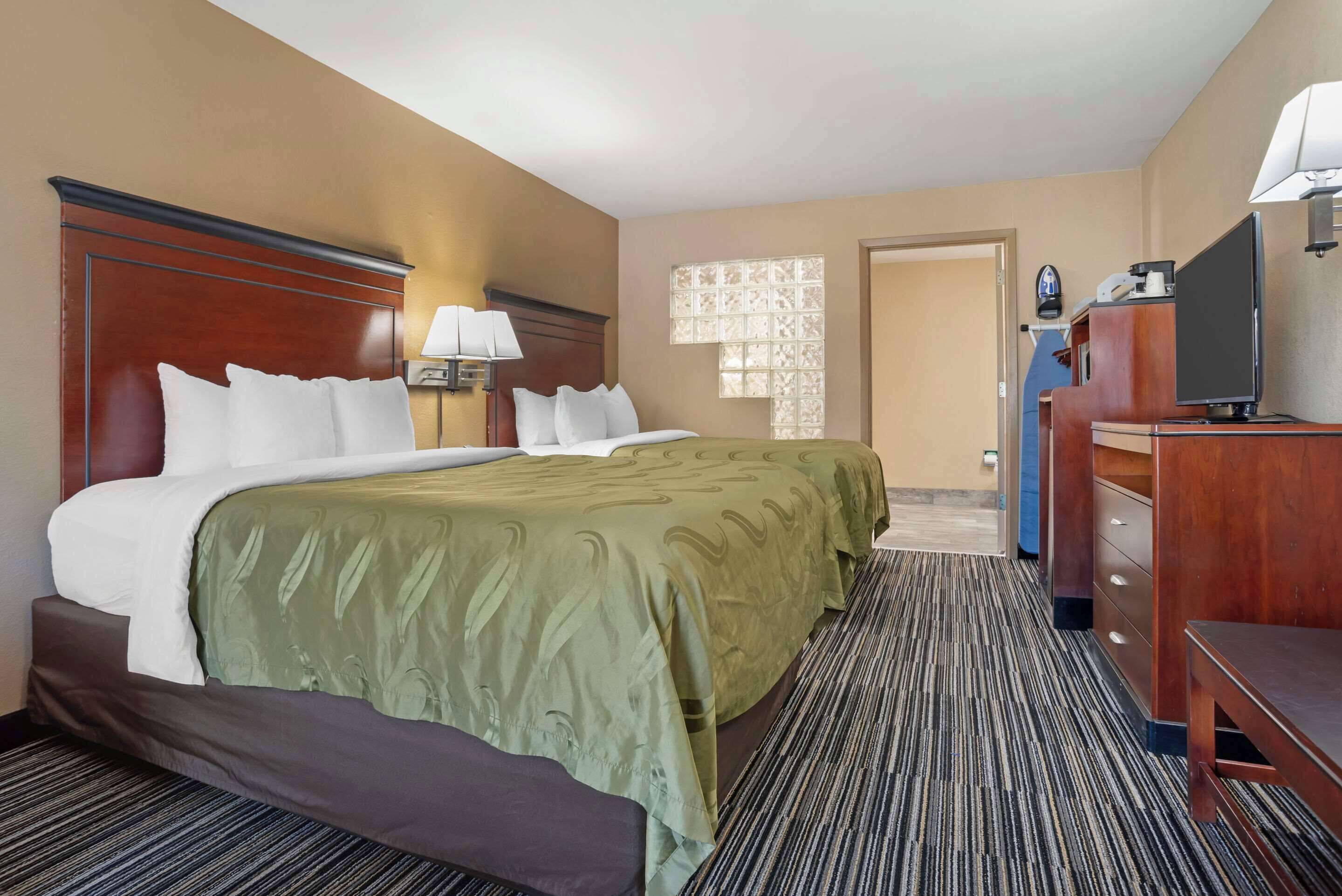 Une chambre d’hôtel avec un grand lit, un bureau, une chaise, une télévision et une fenêtre avec des rideaux à motifs.