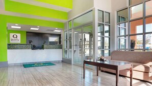 A hotel reception area with a green accent wall, a reception desk, a sofa, and a large window providing a view outside. - Quality Inn Brookhaven (Brookhaven)