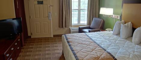 A hotel room with a bed, a television, a desk, a chair, and a window with curtains.