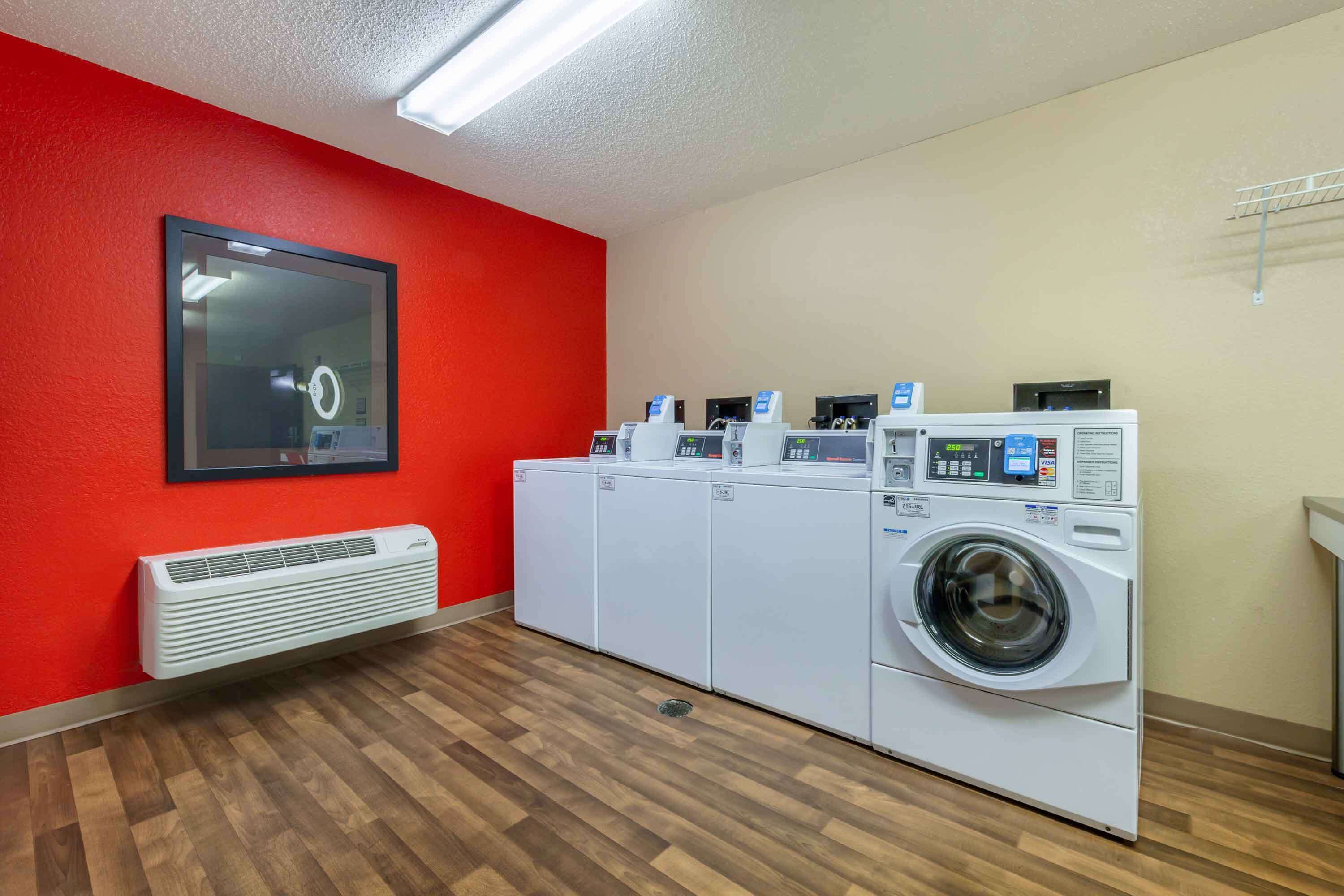 Una sala de bugaderia amb una paret vermella, un mirall gran i diverses rentadores.