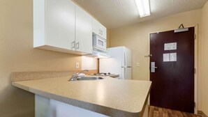A compact kitchen with white cabinets, a microwave, a refrigerator, and a sink.