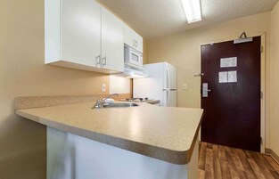 Una cocina funcional con gabinetes blancos, microondas, refrigerador y pileta.