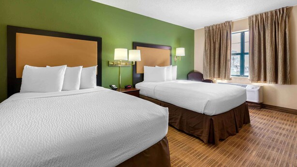 A hotel room with two beds, a desk, a chair, a telephone, and a window with curtains.
