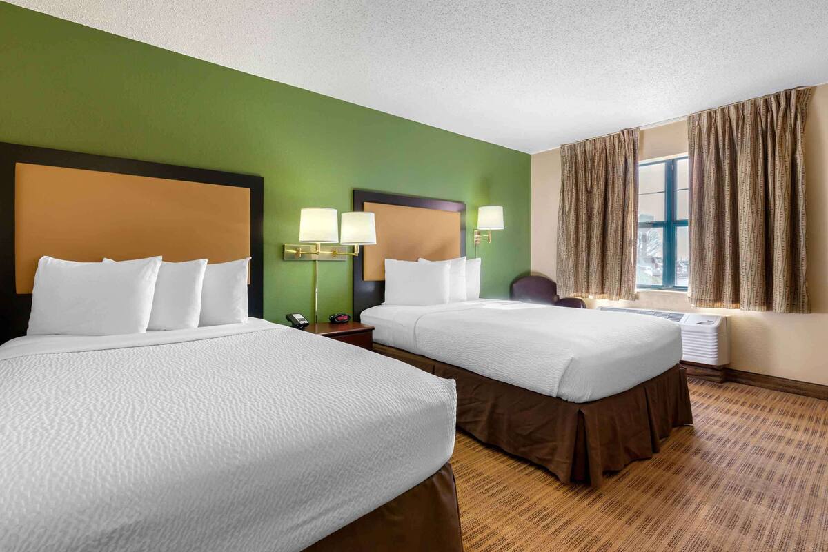 Een hotelkamer met twee bedden, een bureau, een stoel, een telefoon en een raam met gordijnen.