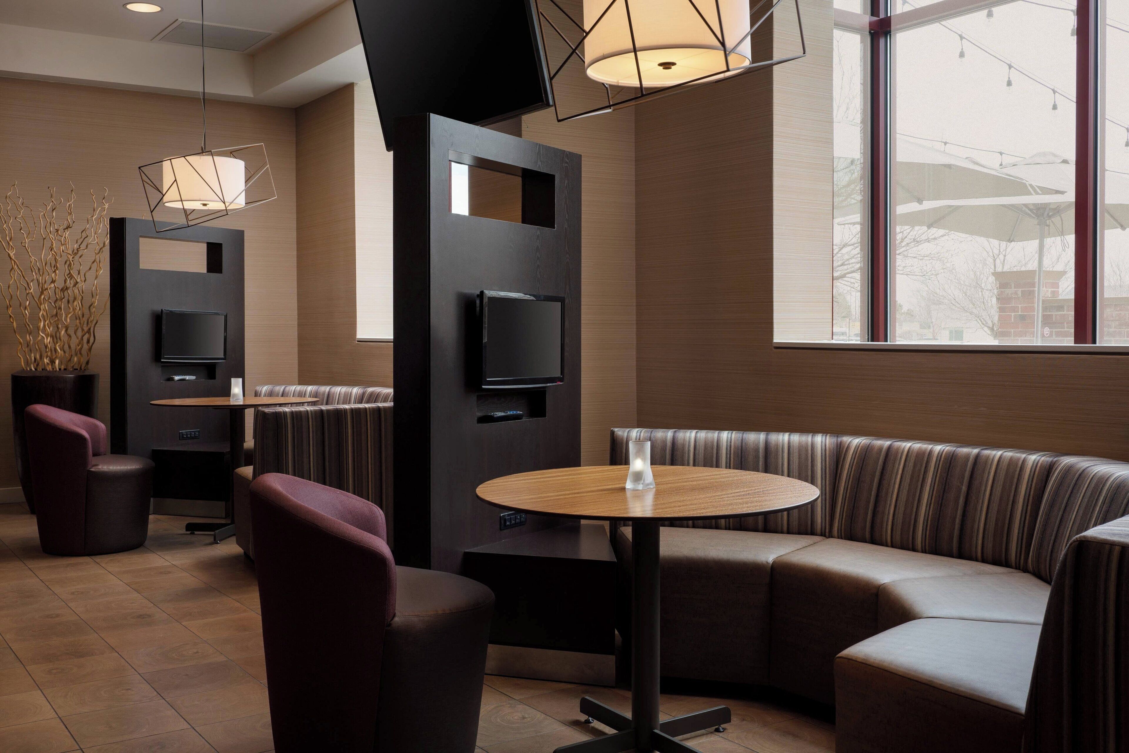 A modern lounge area with a round table, cushioned seating, and a flat-screen TV mounted on a dark panel.