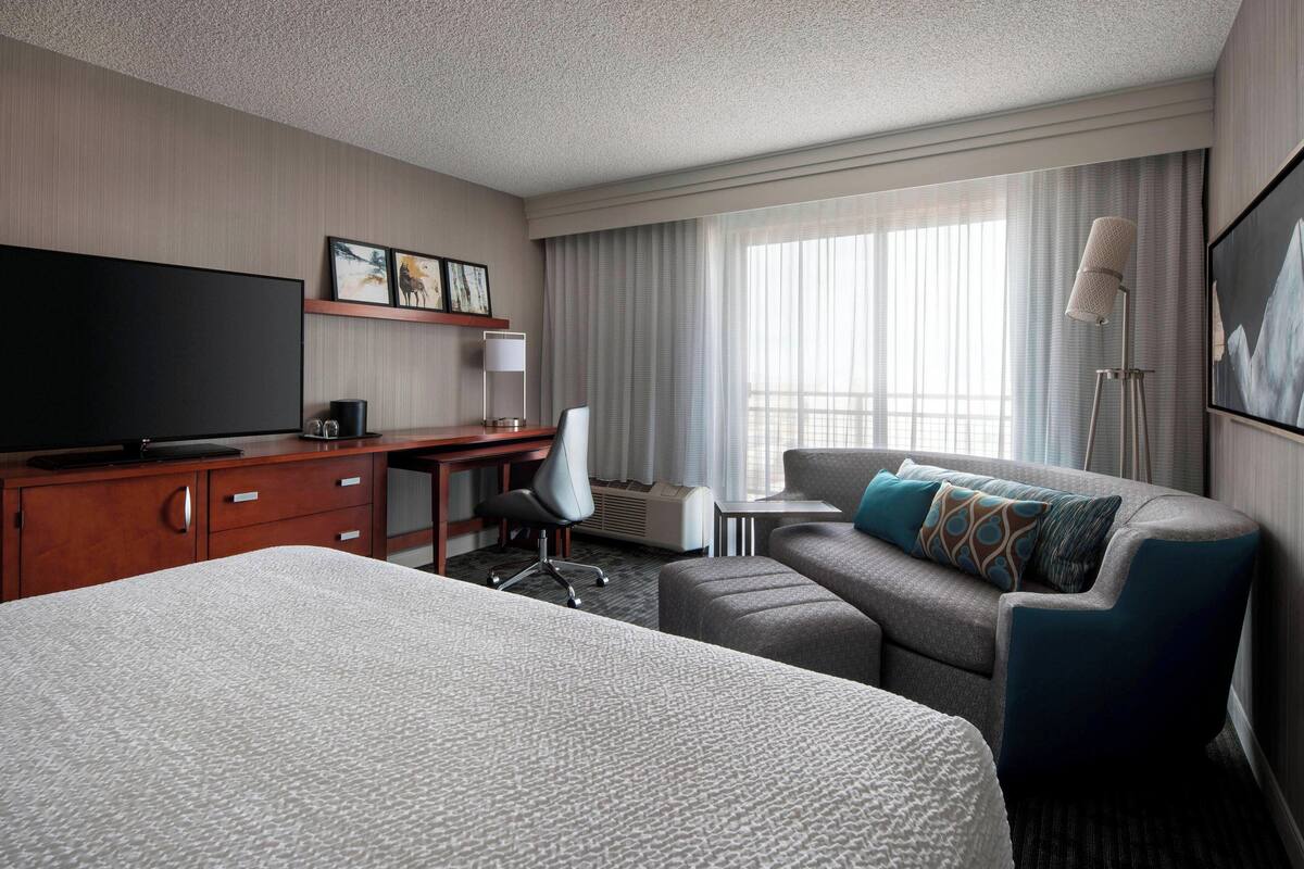 A hotel room with a large bed, a desk with a flat-screen TV, a sofa, and a chair.