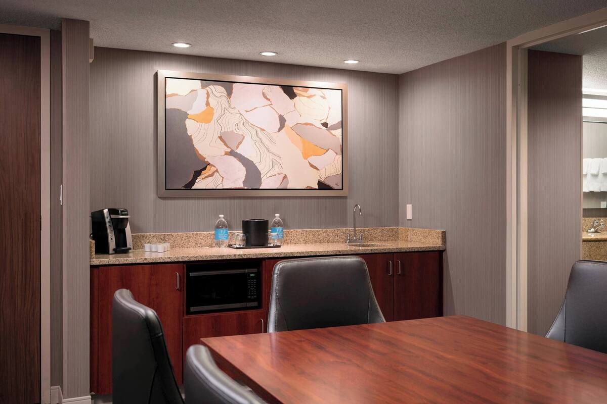 A modern kitchen with a granite countertop, a coffee maker, and a dishwasher. There is a large abstract painting on the wall above the counter.