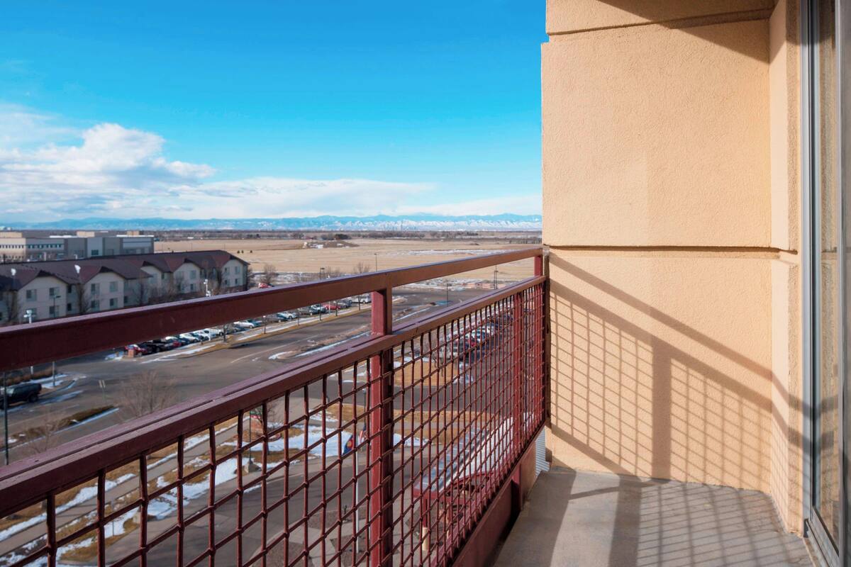 A balcony with a view of a parking lot and distant buildings.