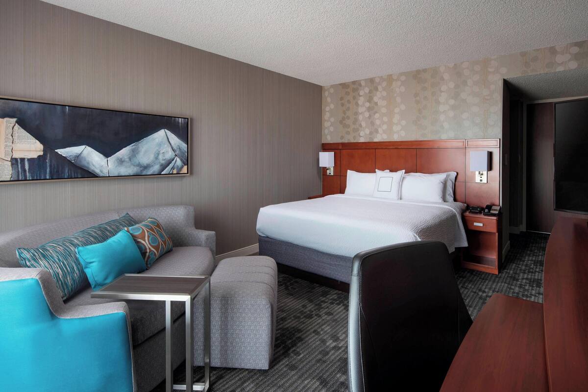 A hotel room with a bed, a sofa, a desk, and a TV.