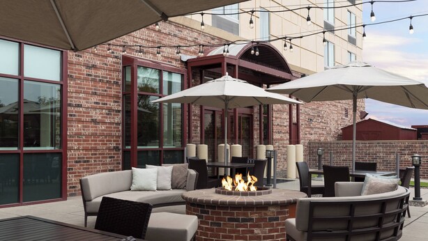 An outdoor patio area with a brick fire pit, seating, and string lights. - Courtyard by Marriott Denver Airport (Denver)