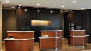A reception area with three wooden reception desks, a wall-mounted digital display, and a ceiling with recessed lighting. - Courtyard by Marriott Denver Airport (Denver)