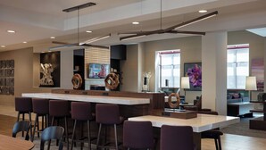 A modern bar area with a long counter, multiple bar stools, and a television screen. - Courtyard by Marriott Denver Airport (Denver)