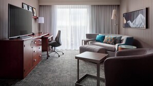 A hotel room with a desk, a television, a sofa, and a coffee table. - Courtyard by Marriott Denver Airport (Denver)