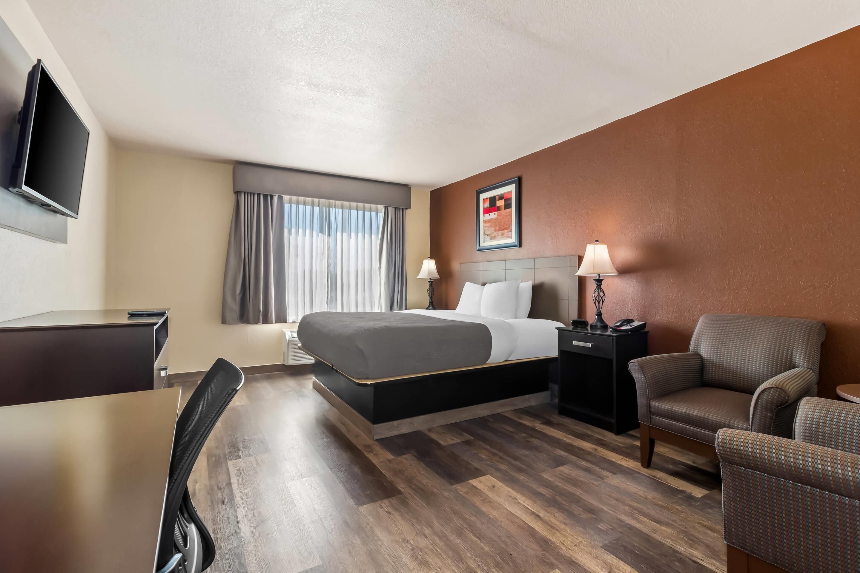 Habitación de hotel con cama, escritorio, silla, televisión y lámpara.