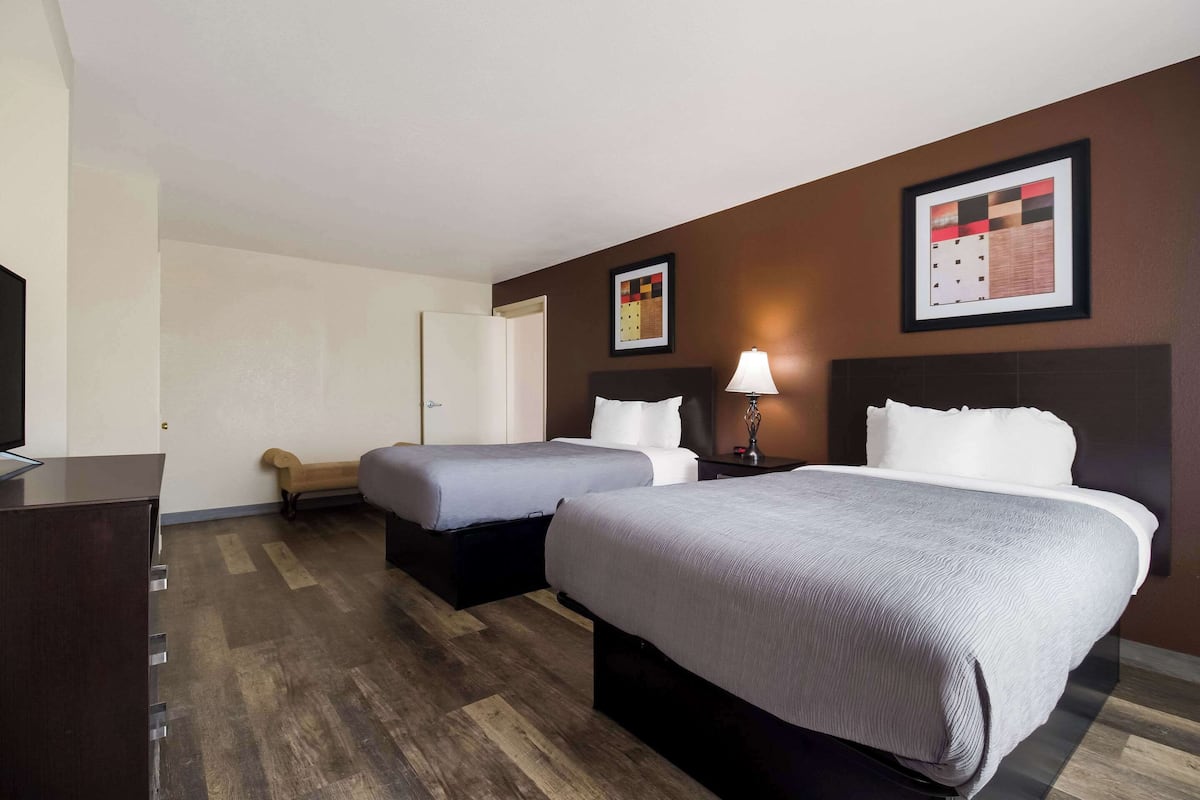 A hotel room with two beds, a desk, a chair, and a TV.