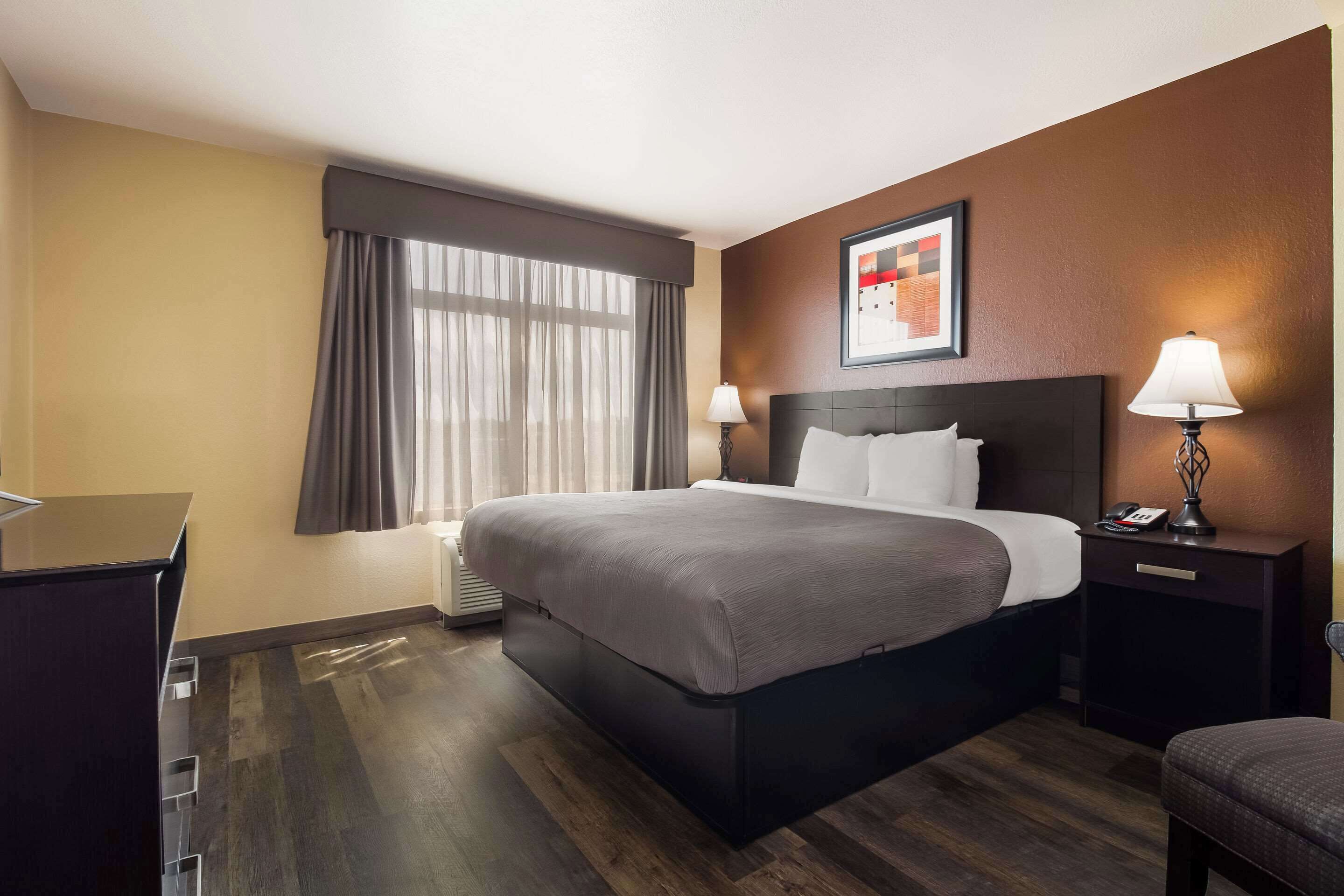 Ein Hotelzimmer mit einem großen Bett, einem Schreibtisch, einem Stuhl, einem Nachttisch mit Lampe und einem Vorhangfenster.