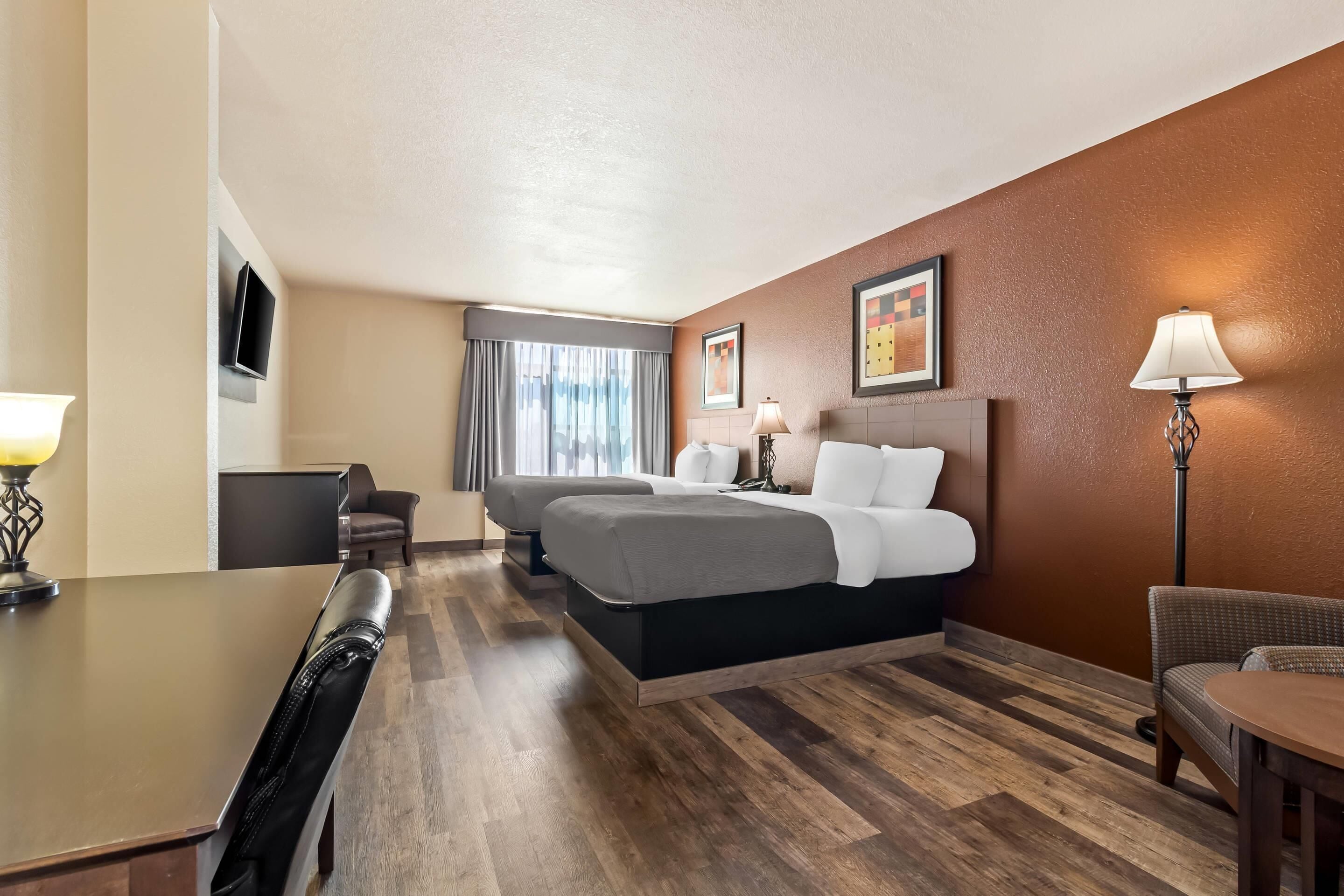 A hotel room with a bed, two bedside tables, a desk, a chair, a lamp, and a TV.