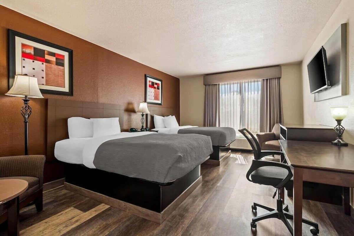 A hotel room with two beds, a desk, a chair, a TV, and a calendar on the wall.