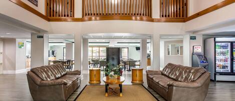 A spacious lobby with two leather sofas, a central coffee table, and a decorative rug. A staircase with wooden railings leads to an upper level.