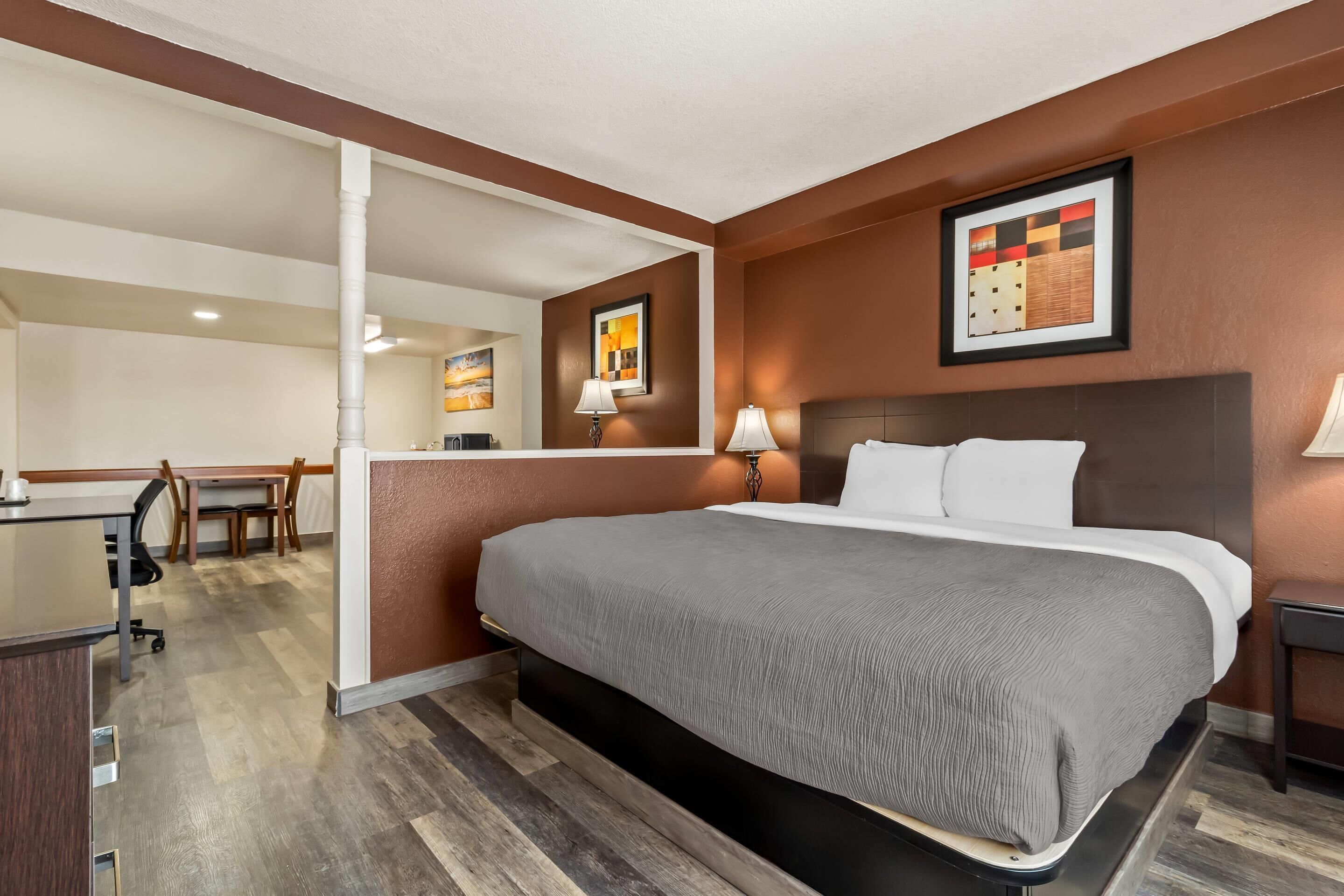 A hotel room with a large bed, a desk, and a chair. There are two wall-mounted lamps and a framed picture on the wall.