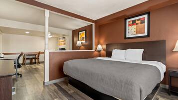 A hotel room with a large bed, a desk, and a chair. There are two wall-mounted lamps and a framed picture on the wall.