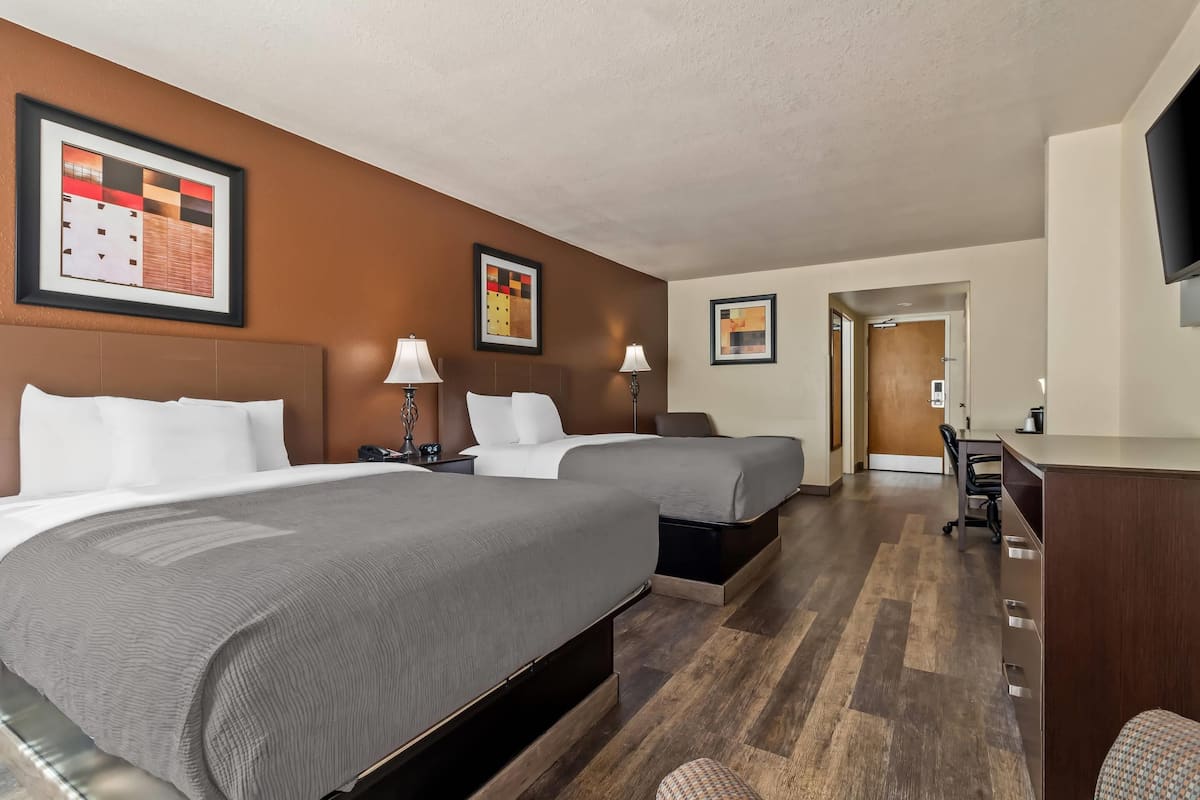 A hotel room with two beds, a desk, and a TV.