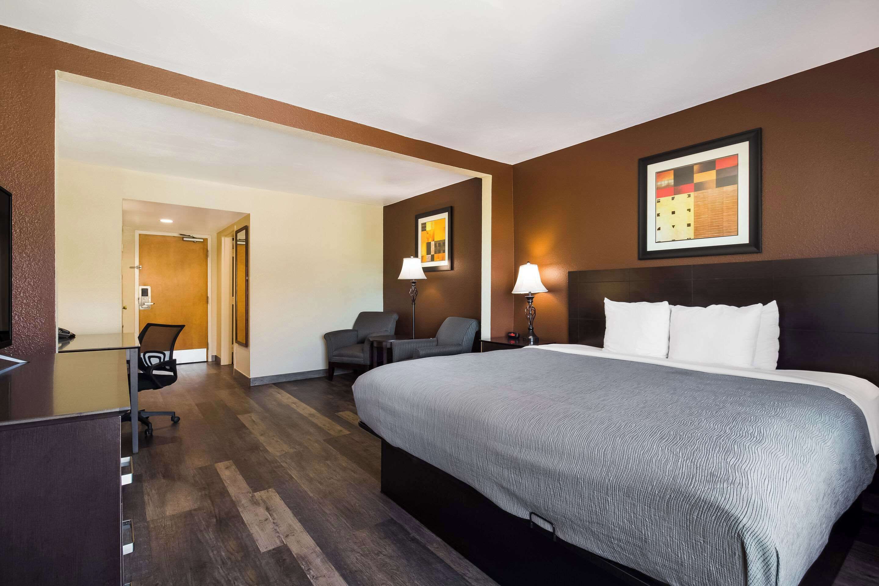A hotel room with a large bed, a desk, a chair, and a lamp.